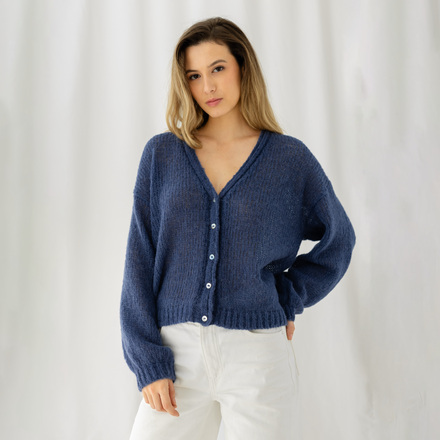 Woman wearing a blue cardigan and white pants against a white background