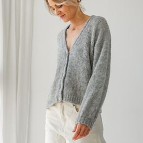 Woman wearing a gray cardigan and white pants against a plain background