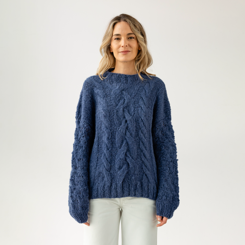 Woman wearing a blue cable knit sweater on a white background