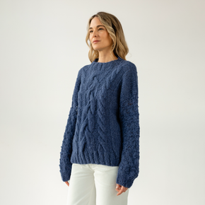 Woman wearing a blue cable knit sweater against a white background