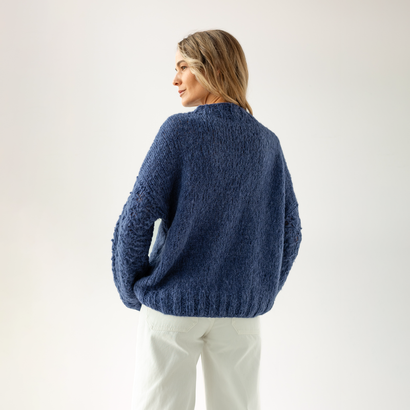 Woman wearing a blue sweater and white pants on a light gray background