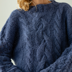 Person wearing a blue cable knit sweater against a light background