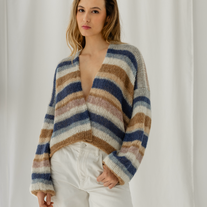 Woman wearing a striped sweater and white pants against a plain background