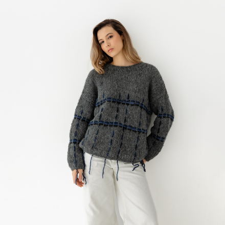 Woman wearing a gray sweater with blue and black accents against a white background