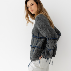 Woman wearing a gray sweater with blue and black accents against a white background