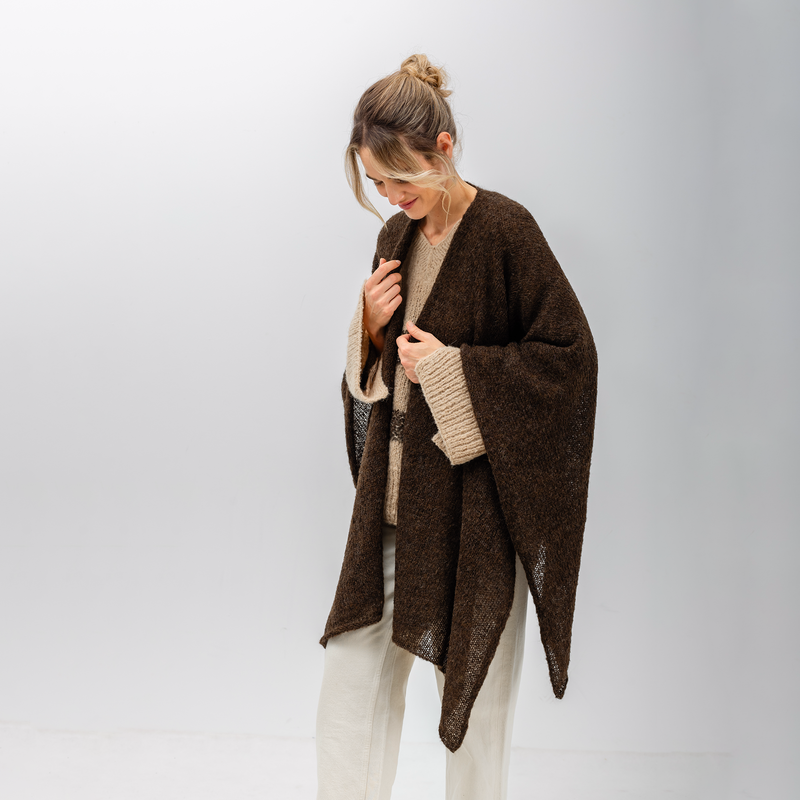 Woman wearing a brown poncho over a beige sweater on a white background