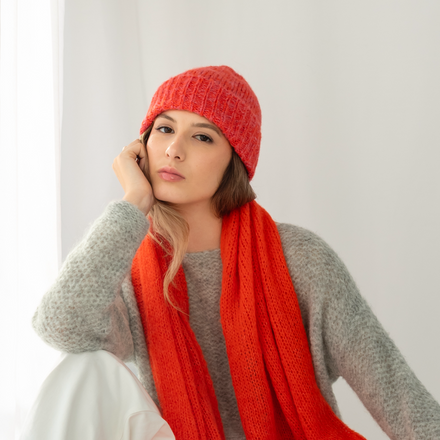 Woman wearing a red knitted hat and shawl against a white background
