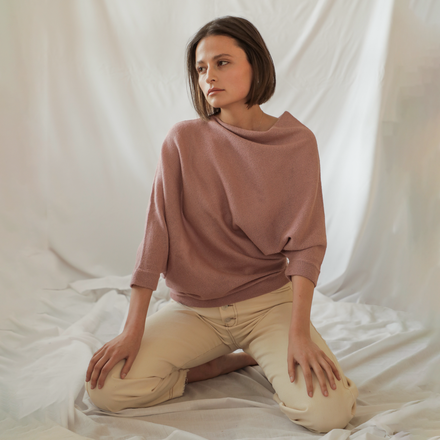 Woman wearing a mauve sweater and beige pants sitting on a white fabric background