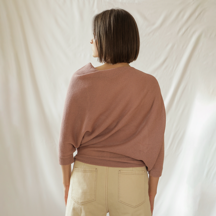 Person wearing a pink sweater and beige pants against a plain background