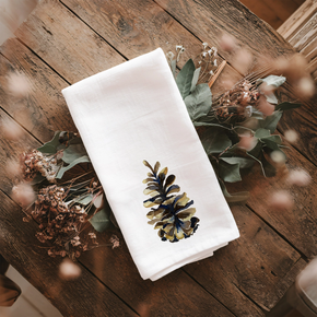 White towel with a pine cone design on a wooden surface with dried flowers.