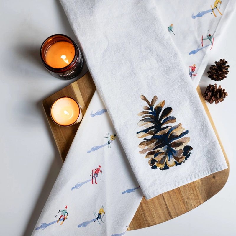 Two white towels with decorative patterns on a wooden board with lit candles.