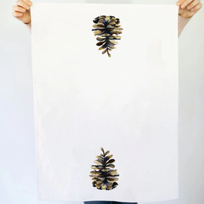 White towel with pine cone design held by hands against a white background