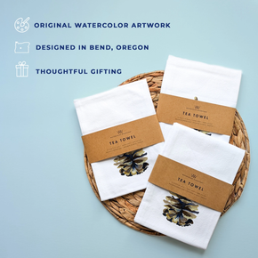 White tea towels with brown packaging on a woven tray against a light blue background