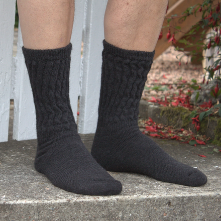 A pair of rib knitted alpaca socks in charcoal, displayed on a person's feet against a white fence and a background with autumn leaves.