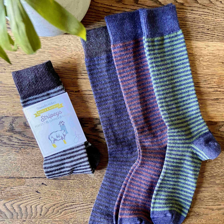 Three pairs of striped socks on a wooden surface with a plant in the corner.