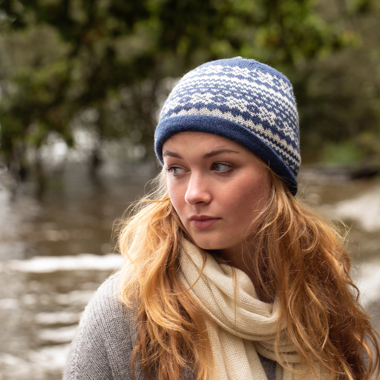 Woman wearing a blue and white patterned knit hat and beige scarf outdoors.