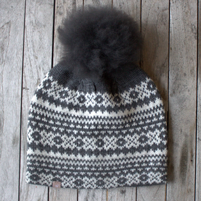 A Fair Isle alpaca knit hat with a detachable alpaca fur pom-pom, displayed on a wooden surface.