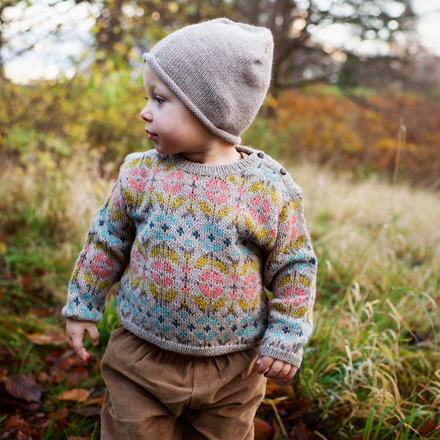 Child wearing a patterned sweater and knit hat standing in a natural setting with blurred background