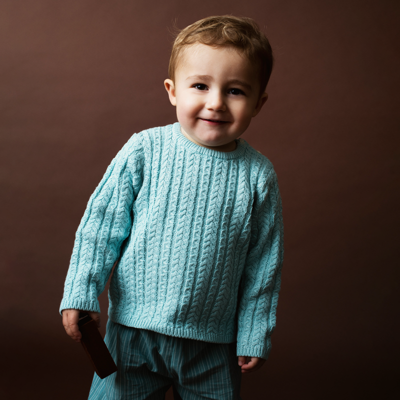 Child wearing a light blue cable knitted sweater against a brown background
