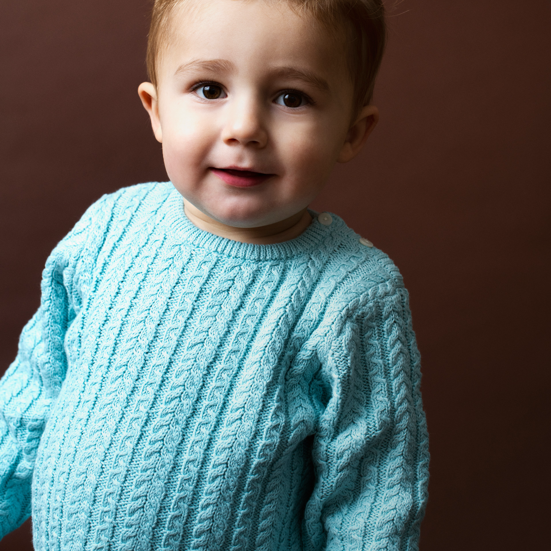 Child wearing a light blue cable knit sweater against a brown background