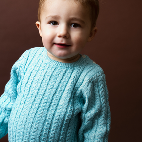 Child wearing a light blue cable knit sweater against a brown background
