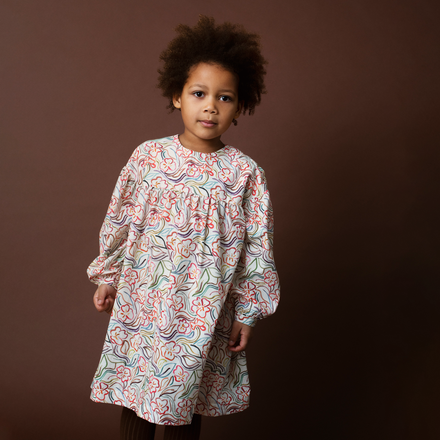 Child wearing a floral patterned dress against a brown background