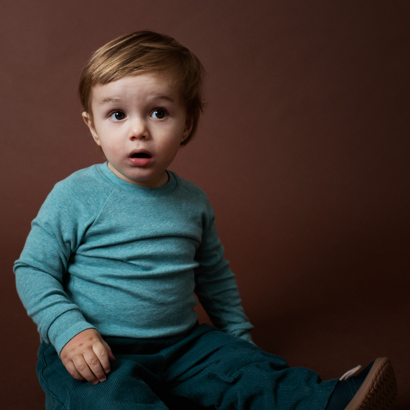 Child wearing a teal outfit sitting on a brown background