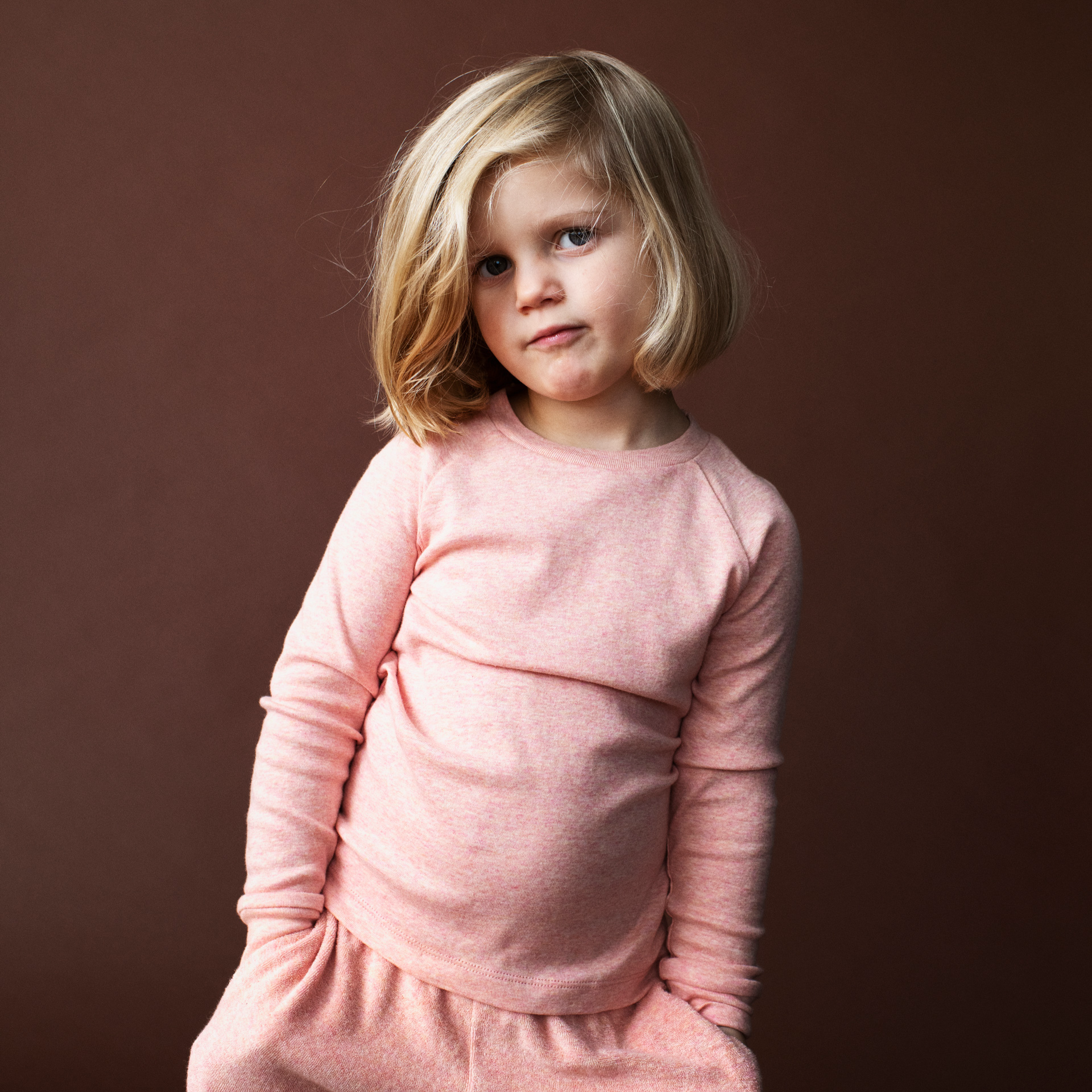Young girl wearing a pink outfit against a brown background