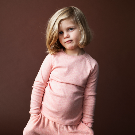 Young girl wearing a pink outfit against a brown background