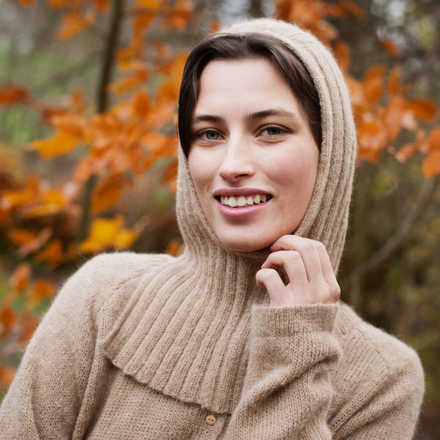 Woman wearing a beige knitted balaclava in an outdoor setting with autumn leaves.