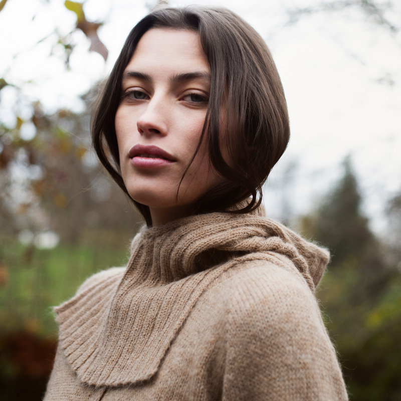 Woman wearing a beige knitted balaclava outdoors.