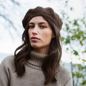Woman wearing a brown beret and sweater outdoors with blurred trees in the background