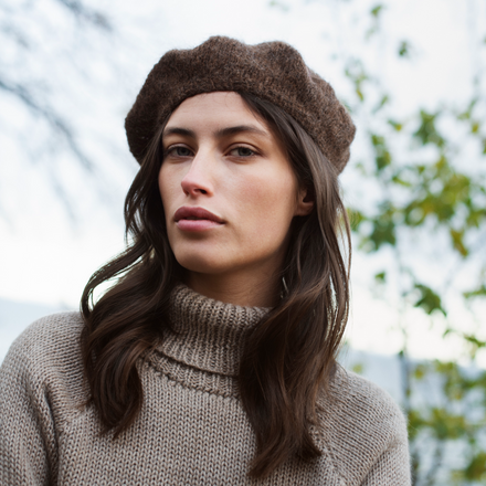 Woman wearing a brown beret and sweater outdoors with blurred trees in the background