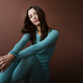 Woman wearing a teal outfit sitting against a brown background