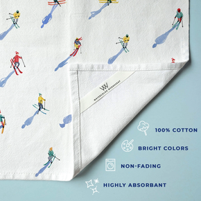 White towel with skiing pattern and Watercolor Wednesday branding on a light blue background