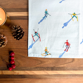 Tea towel with skiing design on a wooden surface with decorative items.
