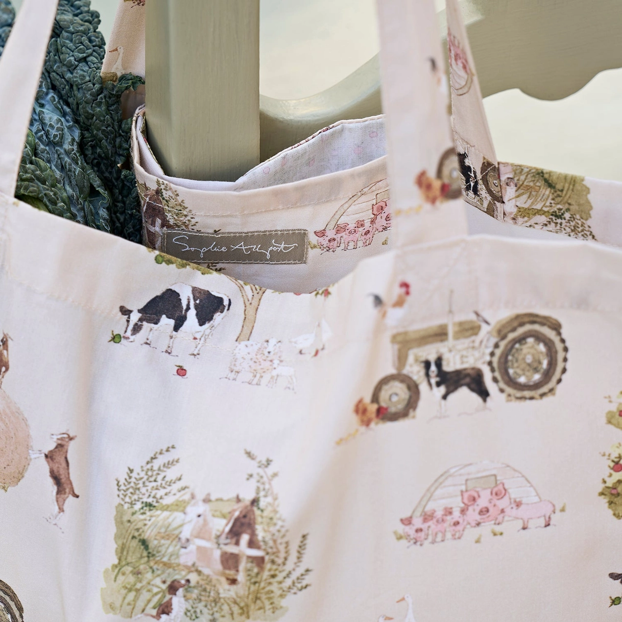 Tote bag with farm-themed design featuring animals and a tractor, held by a person.