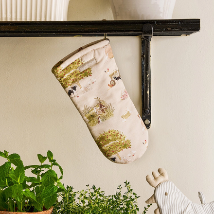 Oven mitt with farm-themed design hanging on a shelf next to potted plants.