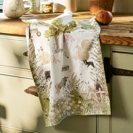 Decorative towel with farm-themed design hanging on a wooden cabinet.