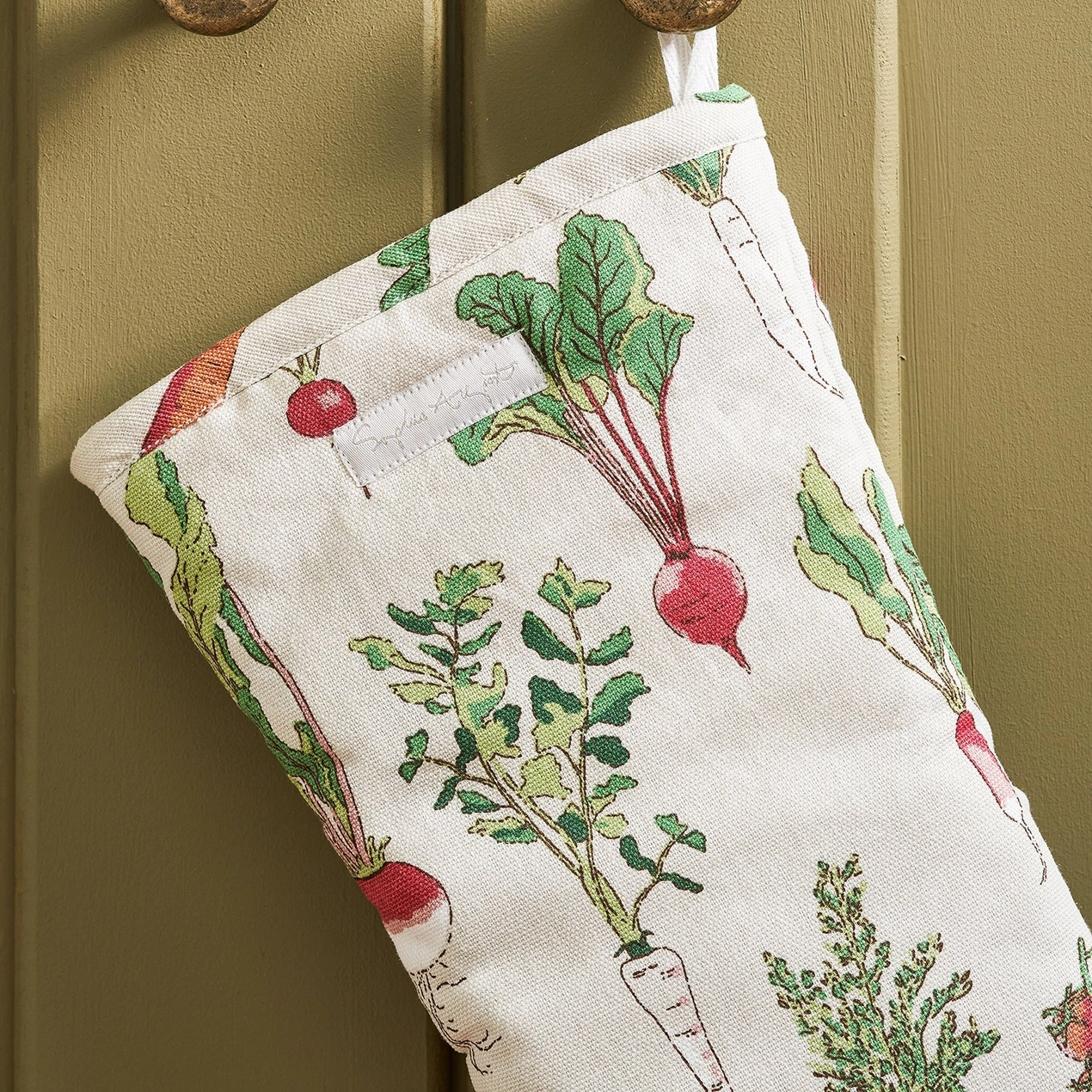 Oven mitt with vegetable pattern hanging on a hook against a beige wall.