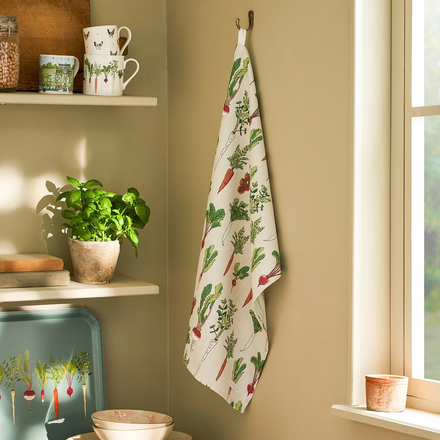 Kitchen towel with vegetable pattern hanging on a wall next to a window