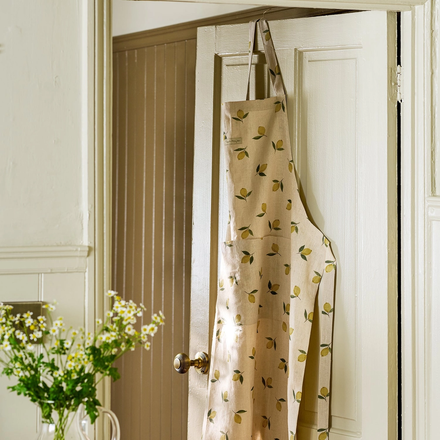 Beige apron with lemon pattern hanging on a white door