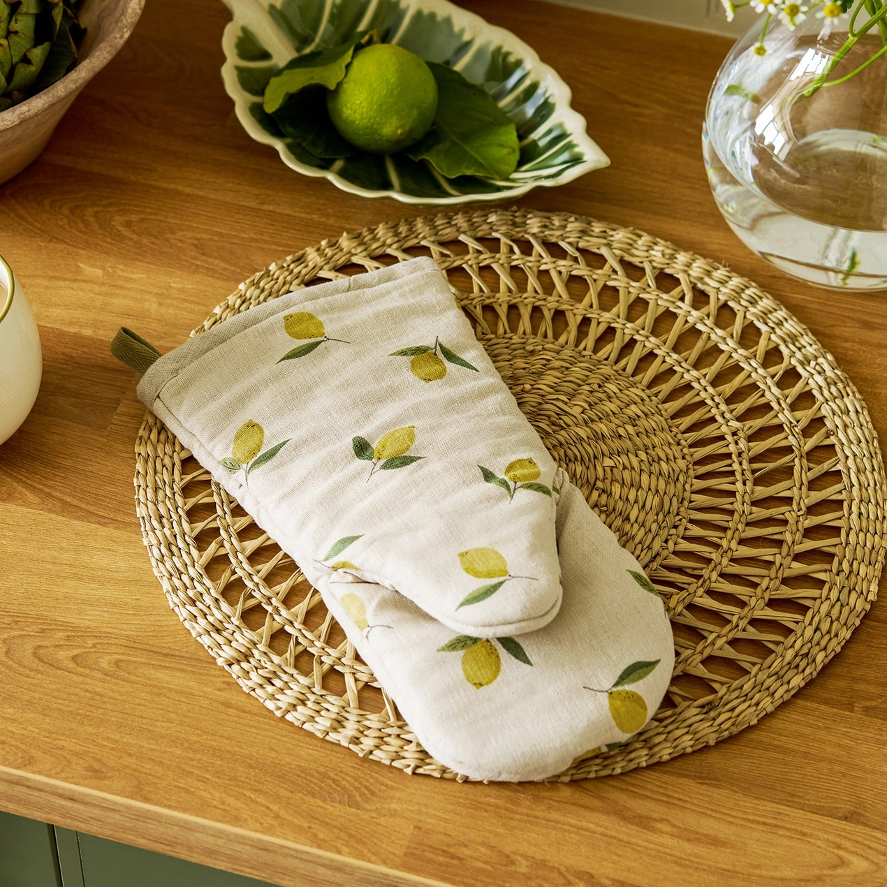 Beige oven mitt with lemon design on a woven mat on a wooden surface