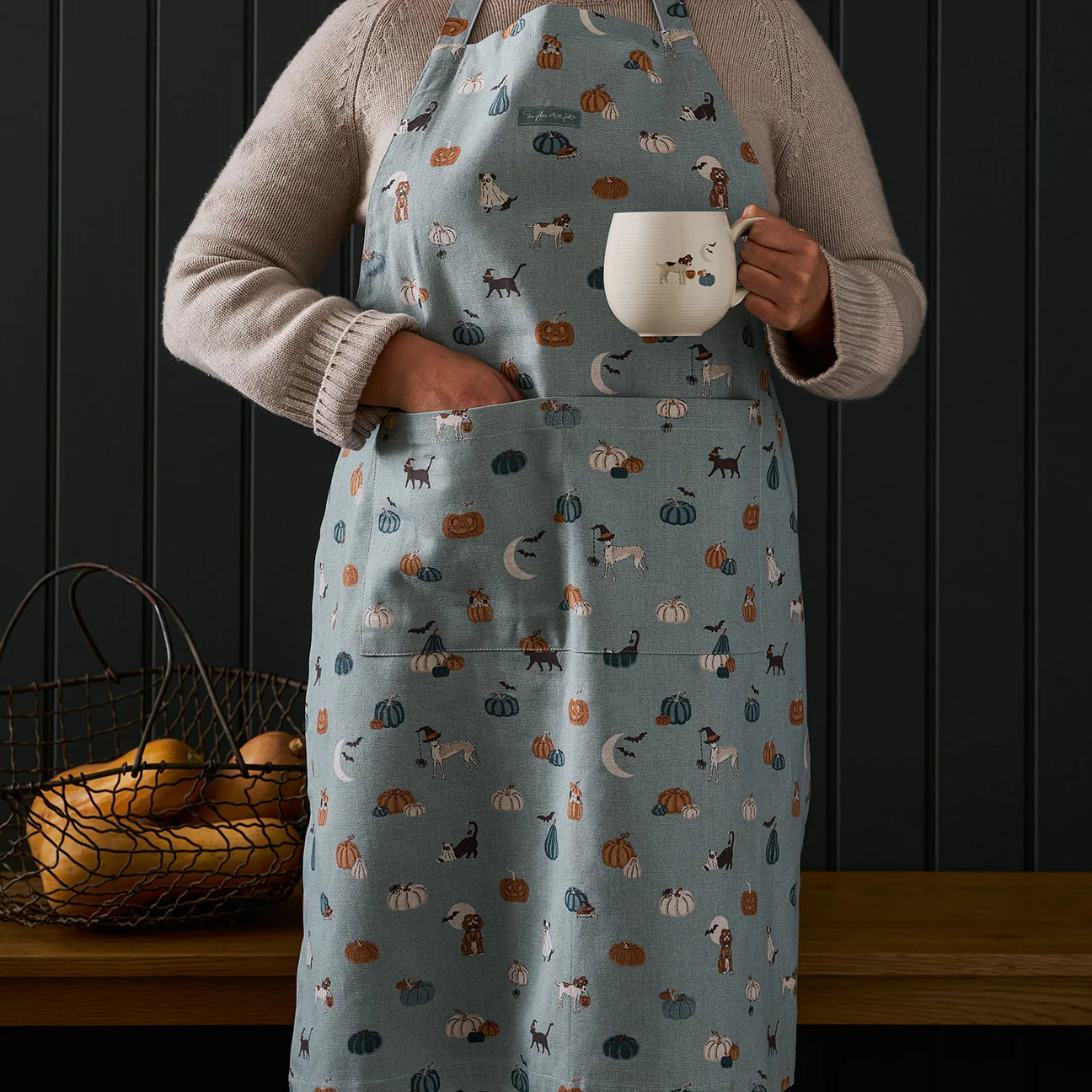 Person wearing a patterned apron holding a mug against a dark wooden background