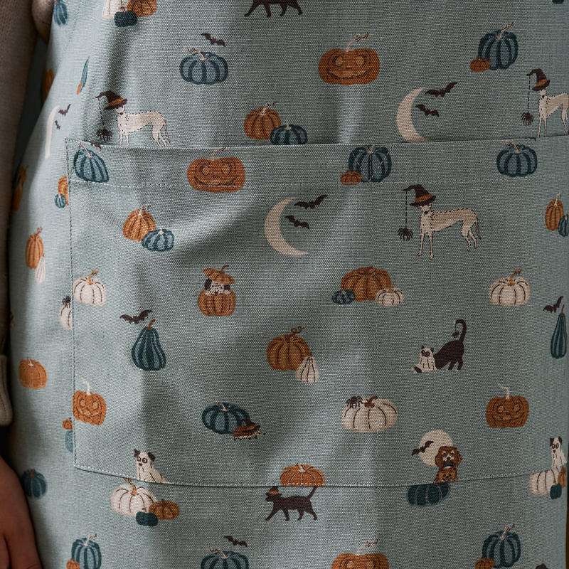 Apron with Halloween-themed pattern featuring pumpkins, ghosts, and cats on a blue background.