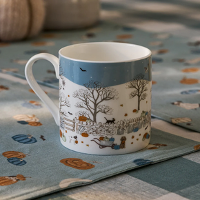White mug with a scenic design on a patterned tablecloth