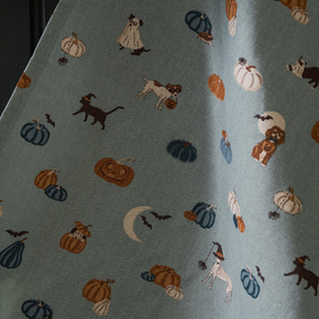 Tea towel with Halloween-themed pattern featuring pumpkins, ghosts, and cats on a blue background.
