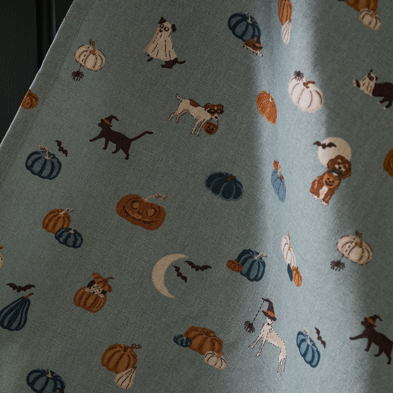 Tea towel with Halloween-themed pattern featuring pumpkins, ghosts, and cats on a blue background.