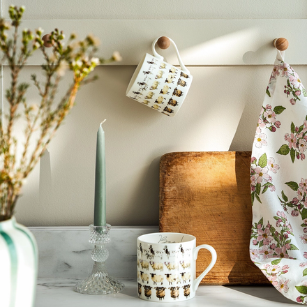 Two mugs with animal pattern, a wooden cutting board, and a floral towel on a neutral background.