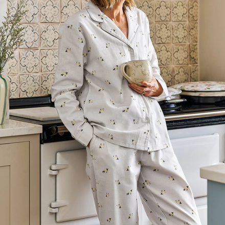 Person wearing a light-colored pajama set with a sheep pattern, holding a mug in a kitchen.